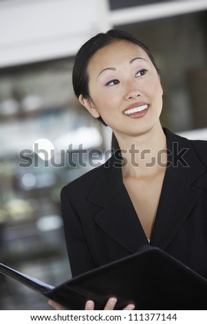Happy businesswoman holding folder and looking away at office