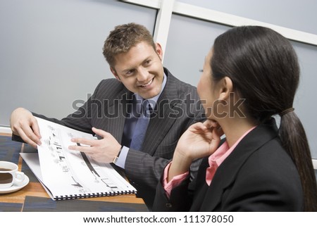 Businessman holding blue print to businesswoman in office