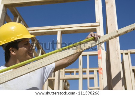 Happy male worker measuring lumber with measure tape at construction site