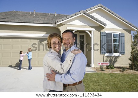 Portrait of happy middle aged couple with daughters in front of new house