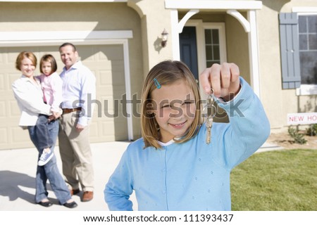Portrait of happy girl with family holding key in front of new house