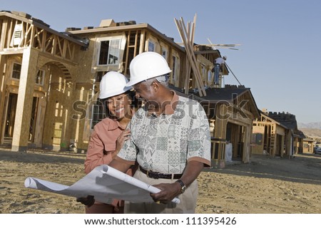 Happy African American senior couple holding blueprint in front of house under construction