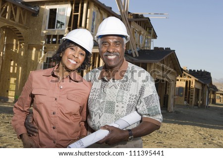 Happy senior couple holding blueprint in front of house under construction