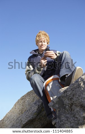 Low angle view of a young man with compass sitting on a rock