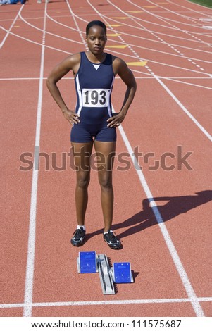 Full length of African American female athlete at starting block on race track