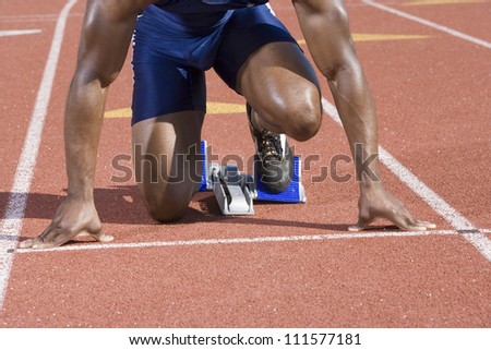 African American male athlete at starting block in race track