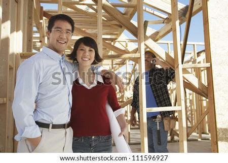 Portrait of a happy Asian couple at construction site with contractor in background
