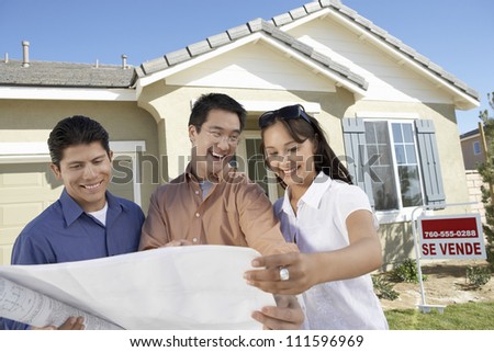 Happy couple with real estate agent reviewing blueprint in front of new house
