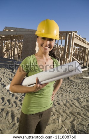 Happy hispanic woman holding rolled up blueprint at construction site