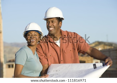 African American couple at construction site holding blueprint