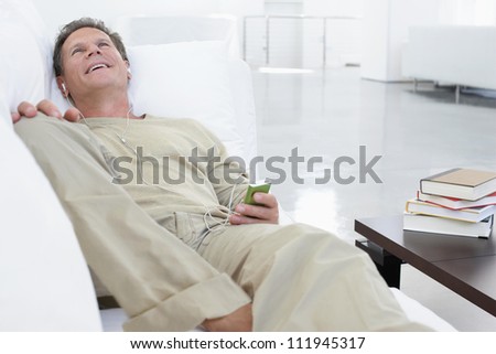 Happy middle aged man lying on couch while listening music