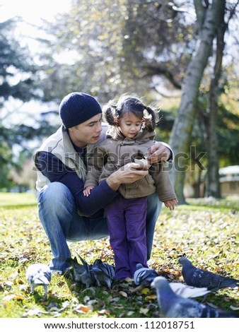 Father and daughter feeding pigeons in the park on sunny day
