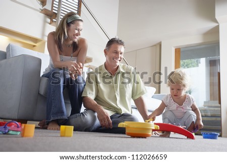Happy parents watching daughter playing with toy