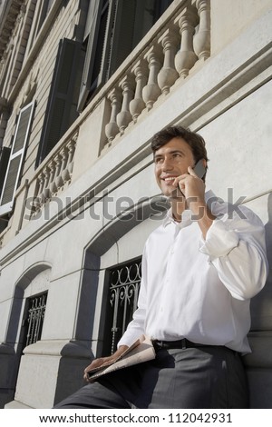 Businessman communicating on cell phone while leaning on the wall