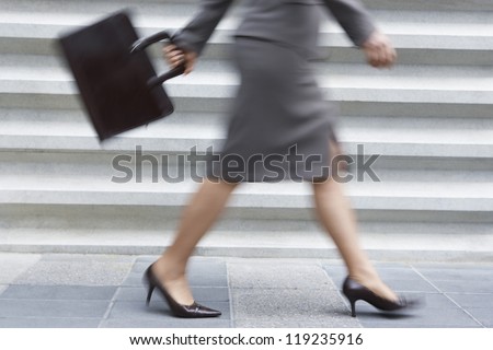 Blurred motion of the low section of a businesswoman in high-heels carrying laptop bag