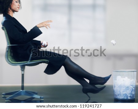 Businesswoman on chair throwing paper ball into dustbin