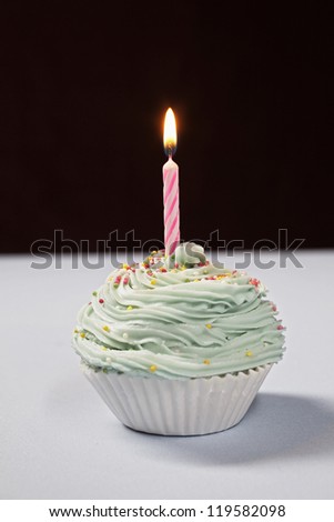 Decorated cupcake on table with lighted candle isolated over black background