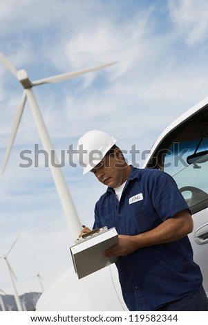 Male architect noting down on clipboard at wind mill farms