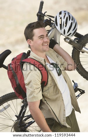 Happy Caucasian male cyclist carrying bicycle while looking away