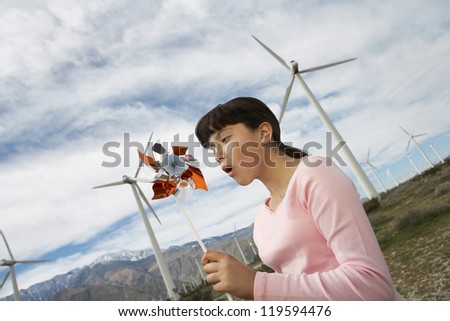 Teenage girl playing with paper windmill at wind farm