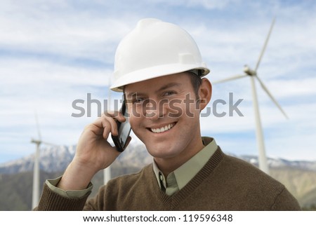 Portrait of a happy male engineer using cell phone at wind farms