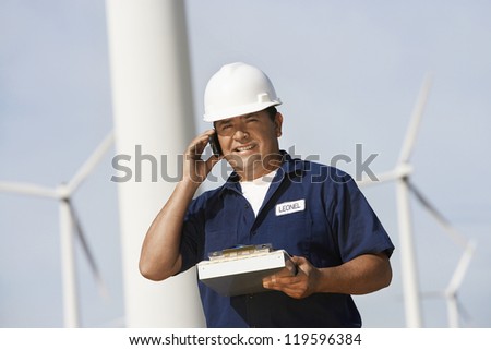 Male engineer on call with clipboard at wind farm