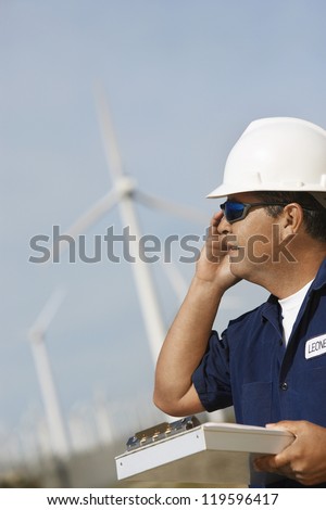 Mature engineer on call with clipboard at wind farm