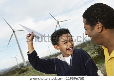 Mature man looking at son playing with paper plane at wind farm