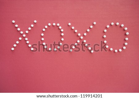 Close-up of push pins in formation of x and o over pink background depicting hugs and kisses
