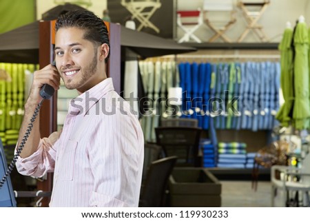 Portrait of handsome young employee in store listening to telephone receiver