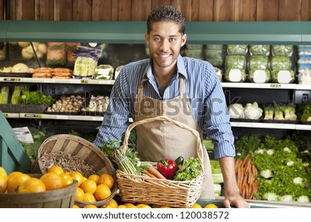 Portrait of a happy young salesman with vegetable basket in supermarket