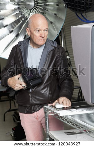 Middle Age photographer with camera using computer in studio