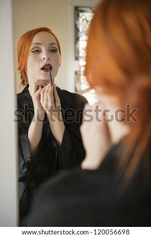 Young female applying lip liner in front of mirror