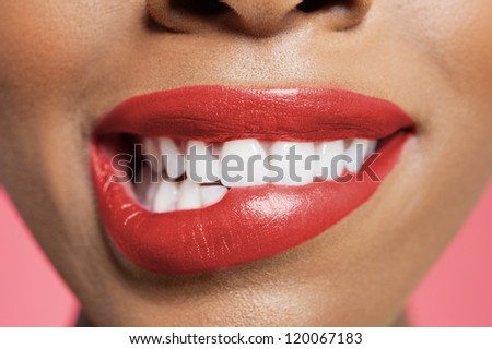 Close-up view of an female biting her red lip over colored background