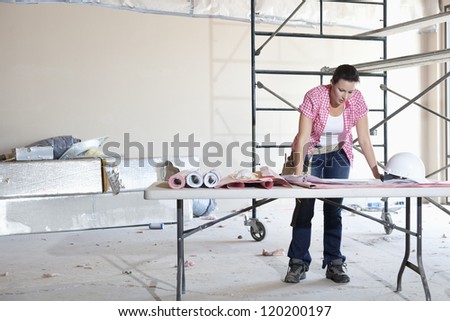 Front view of young female contractor looking at building plans at table