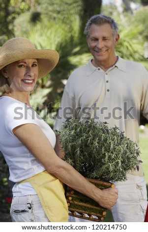 Portrait of a senior woman holding plant with man standing in the background