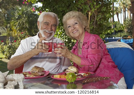 Portrait of a happy senior couple toasting glasses of drink while having food in an open restaurant