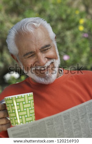 Happy senior man reading newspaper while having tea at lawn