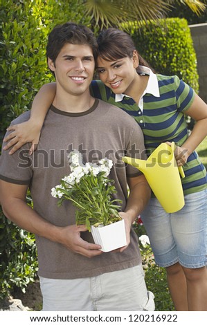 Portrait of a happy brother and sister standing together while holding flower pot and  watering can at garden