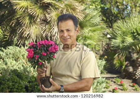 Portrait of a happy middle aged man holding flower plant at lawn