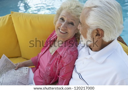 High angle view of a senior happy couple sitting together on sofa with swimming pool in the background