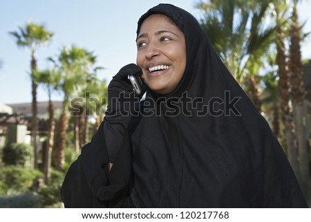 Happy Indian woman in burka communicating on mobile phone