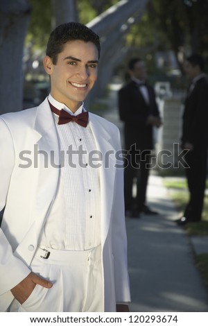 Portrait of a handsome young groom standing with two male friends in the background