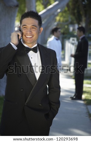 Happy Hispanic groom communicating on phone with two male friends standing in the background