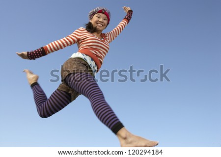 Motion blur low angle view shot of a happy woman jumping with arms outstretched against blue sky