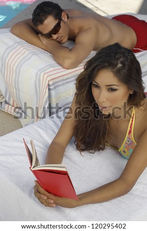 Couple relaxing on lounge chair while woman reading magazine at resort
