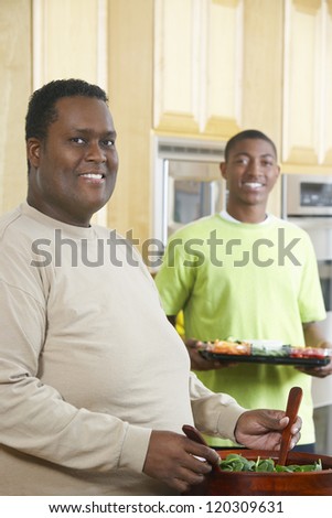 Portrait of an obese African American man preparing salad in kitchen with boy standing in background