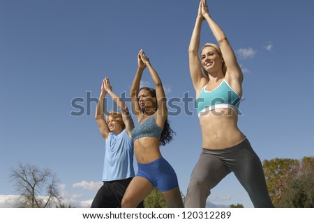 Low angle view of three friends exercising against blue sky