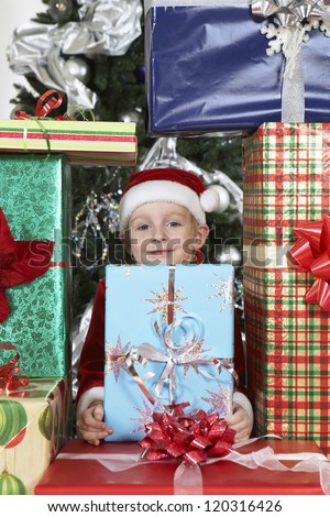Portrait of a preadolescent boy surrounded by gift boxes in Santa Claus outfit