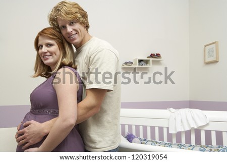 Side view of a happy husband embracing pregnant wife with cradle in the background